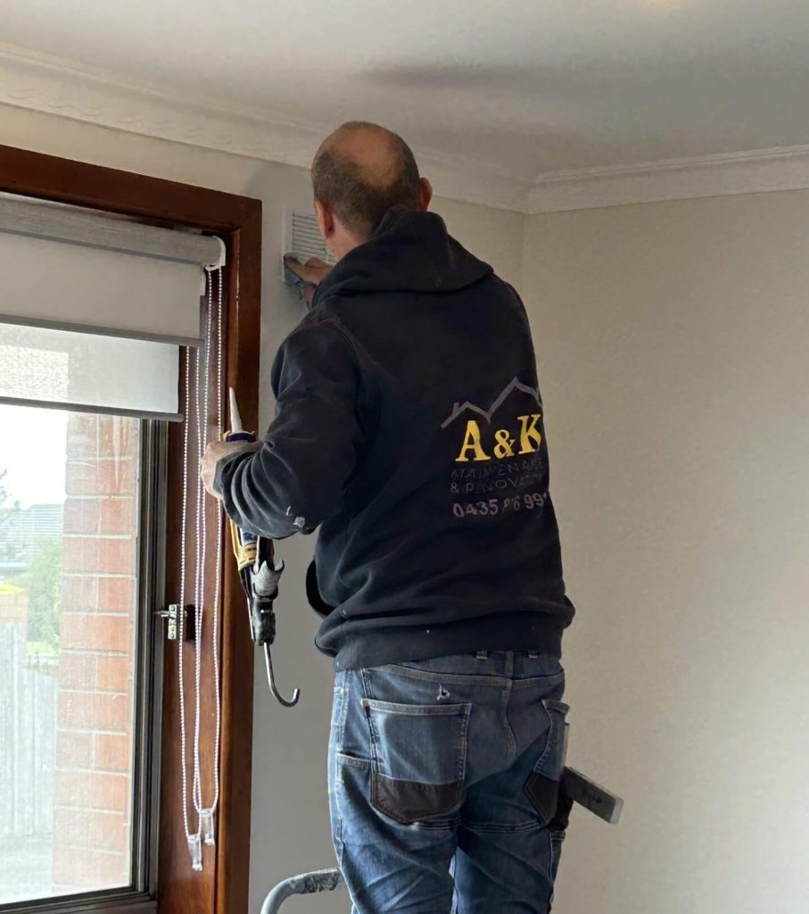 Andy Morgione on a stepladder caulking an air vent inside a house